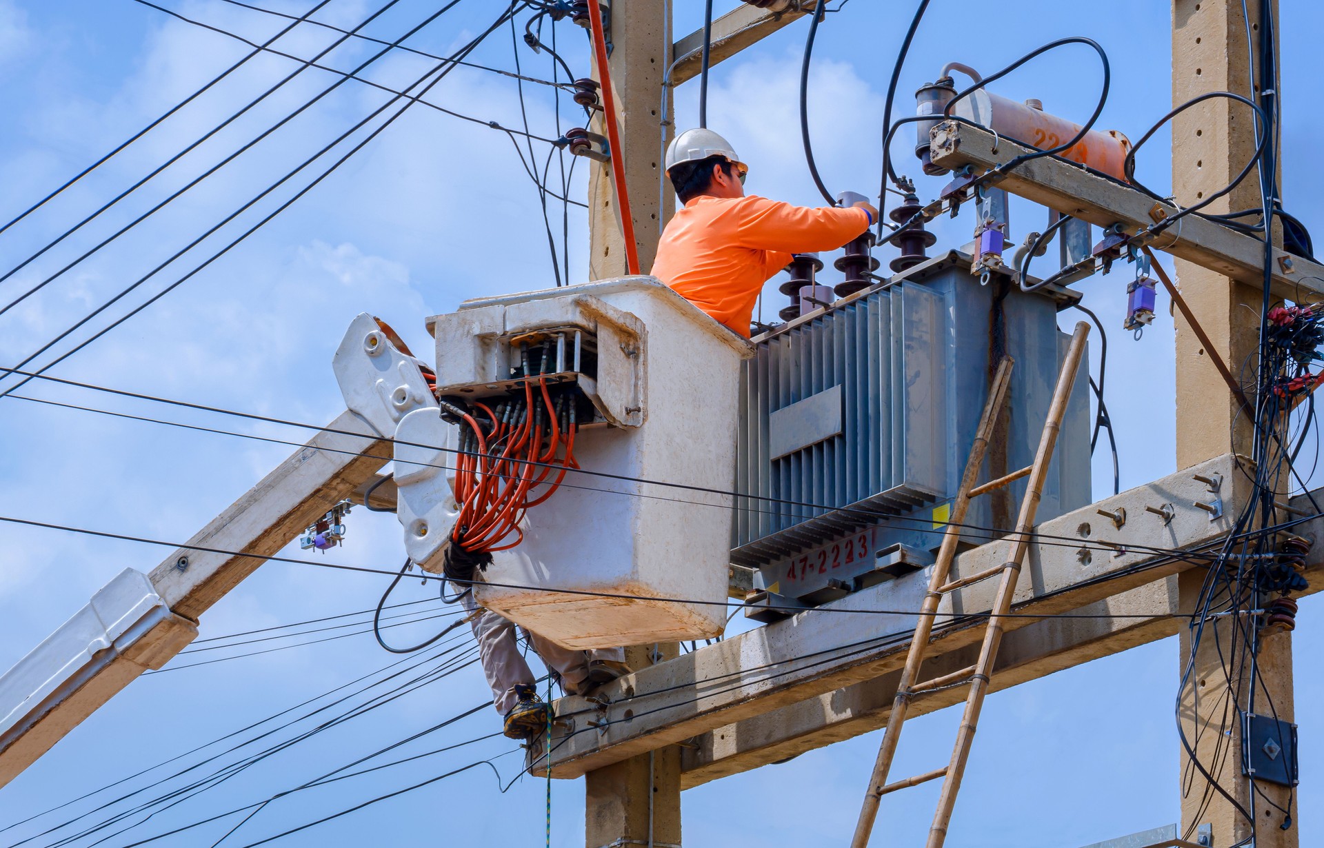 Electrician in bucket of articulated boom lift is repairing electrical transmission on power poles